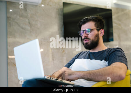 Photo bearded banker working in a modern office overtime. Man sitting in yellow chair at night. Using contemporary laptop, blurred background. Soft li Stock Photo