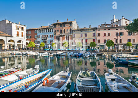ITALY LAKE GARDA DESENZANO DEL GARDA EARLY MORNING THE HARBOUR WITH BOATS AND SURROUNDING COLOURED HOUSES AND RESTAURANTS IN APRIL Stock Photo