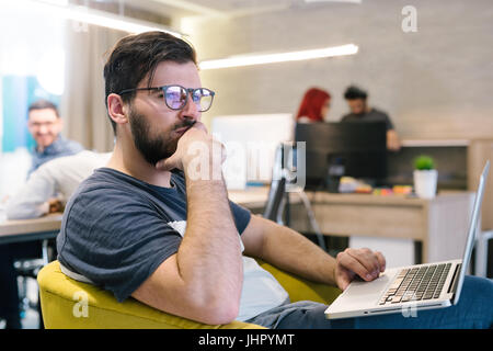 Photo bearded banker working in a modern office overtime. Man sitting in yellow chair at night. Using contemporary laptop, blurred background. Soft li Stock Photo