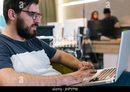 Photo bearded banker working in a modern office overtime. Man sitting in yellow chair at night. Using contemporary laptop, blurred background. Soft li Stock Photo