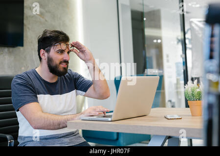 Photo bearded banker working in a modern office overtime. Man sitting in yellow chair at night. Using contemporary laptop, blurred background. Soft li Stock Photo