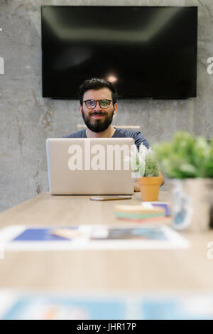 Photo bearded banker working in a modern office overtime. Man sitting in yellow chair at night. Using contemporary laptop, blurred background. Soft li Stock Photo