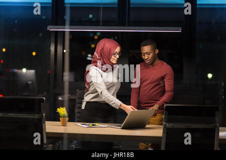 Arab woman and African man collaborating in the office working overtime. Stock Photo