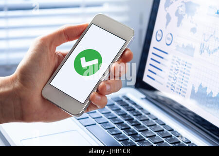 Hand holding a smartphone with a green checkmark icon on the screen to show a validated, confirmed, completed or approved status Stock Photo