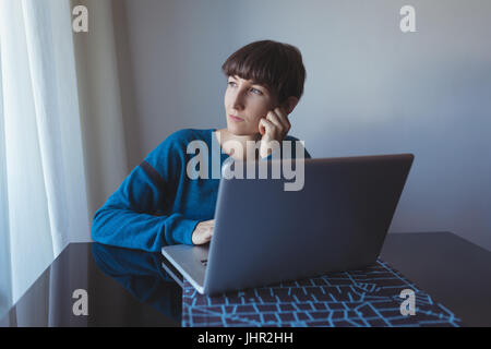 Thoughtful woman using laptop in living room at home Stock Photo