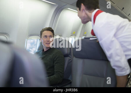 Air hostess interacting with passenger while travelling in an aircraft Stock Photo