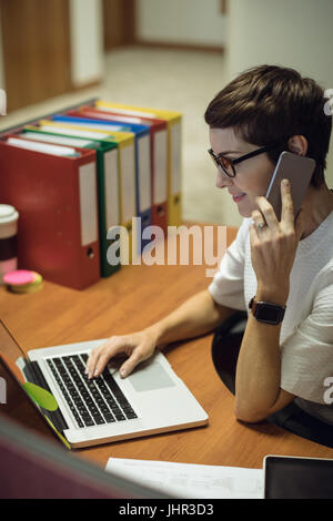 Beautiful businesswoman talking on mobile phone while using laptop in office Stock Photo