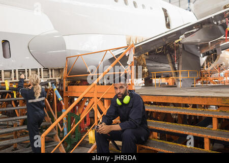 Female aircraft maintenance engineers working over an aircraft while colleague relaxing at airlines maintenance facility Stock Photo