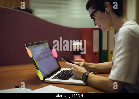 Businesswoman using mobile phone while working on laptop in office Stock Photo