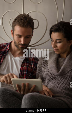 Young couple using tablet computer while sitting on bed at home Stock Photo