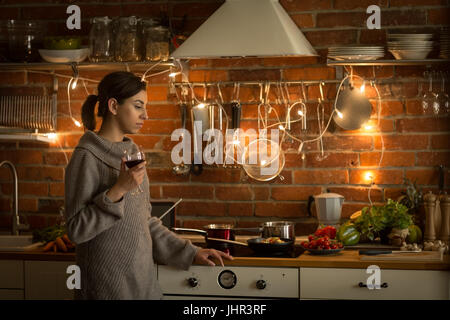 thoughtful woman having wine while standing in kitchen at home Stock Photo