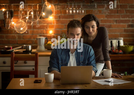 Young couple using laptop at table in kitchen Stock Photo