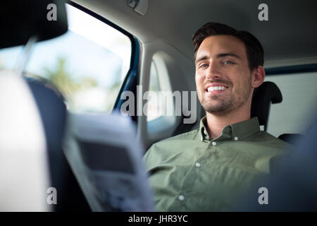 Portrait of smiling man sitting on car with newspaper Stock Photo