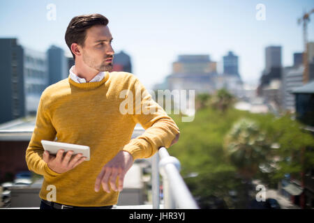 Man standing on balcony with digital tablet on a sunny day Stock Photo