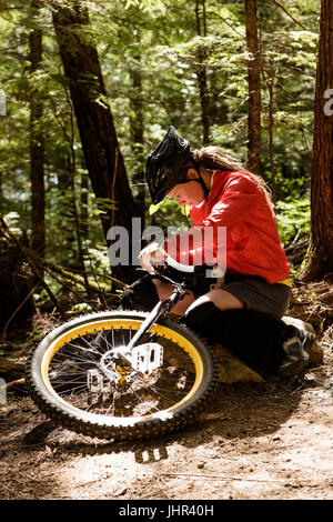 Young woman adjusting unicycle while sitting on rock against trees Stock Photo