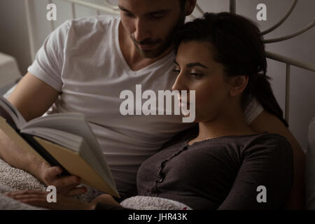Close up of young couple reading book while relaxing on bed at home Stock Photo