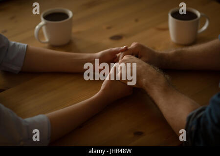 Cropped image of couple holding hands while sitting at table with coffee cup Stock Photo