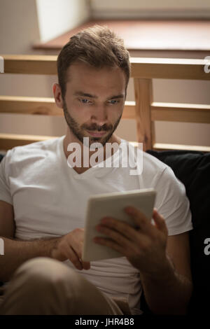 Young man using tablet computer while sitting on bed at home Stock Photo