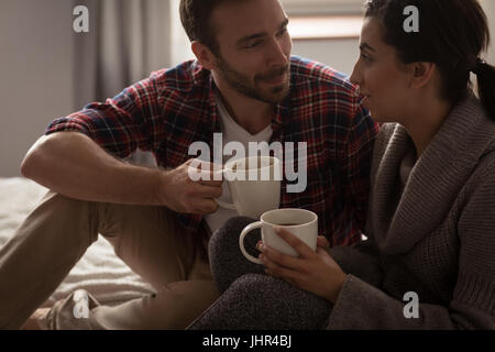 Happy couple having coffee while sitting on bed in bedroom at home Stock Photo