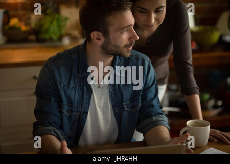Couple talking while using laptop at table in kitchen Stock Photo