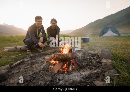 Young couple preparing sausage on campfire at campsite Stock Photo