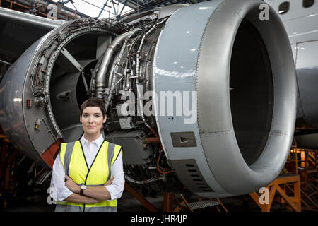 Portrait of female aircraft maintenance engineer standing with arms crossed at airlines maintenance facility Stock Photo