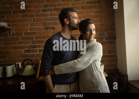 Couple embracing while looking thought away in kitchen at home Stock Photo