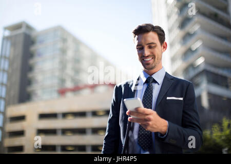 Smiling businessman using mobile phone near office building Stock Photo