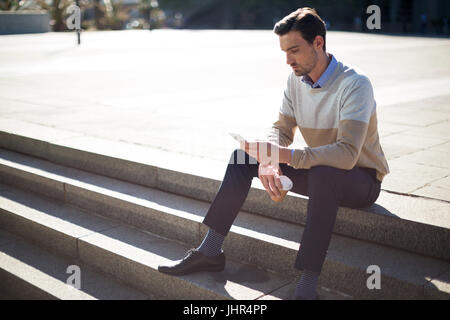 Executive sitting on staircase and using mobile phone in campus Stock Photo