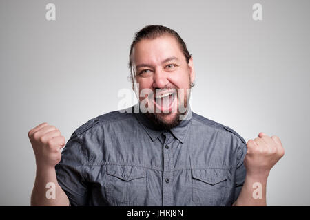 I won Happy young man gesturing and smiling while standing against gray background Stock Photo