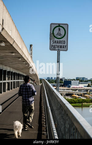 A Shared Pathway sign and a boy with his dog walking on North Arm Canada Line skytrain bridge over the Fraser river between Richmond and Vancouver Stock Photo