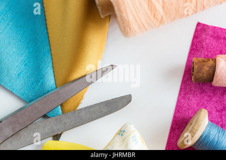 tailoring, sewing, patchwork and fashion concept - closeup tools on white work desk in studio, scissors, spools of blue and pink threads, meter, piece Stock Photo