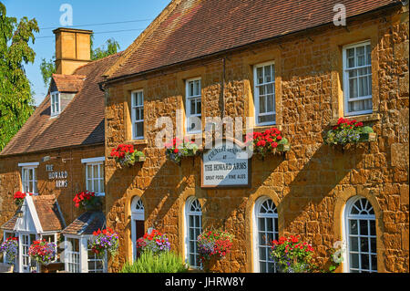 Colourful hanging baskets on the front of a Cotswold stone public house, in the Warwickshire village of Ilmington Stock Photo