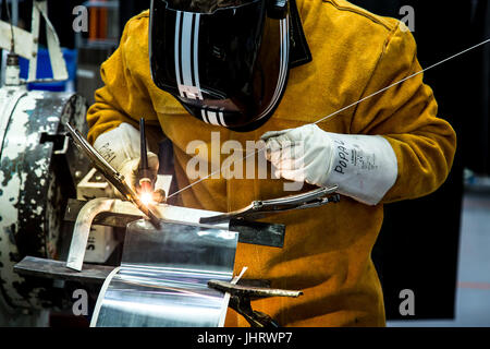 A welder working on a metallic part in an industrial environment wearing a protective mask Stock Photo