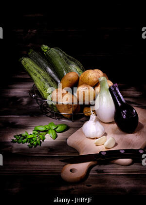 Potatoes, zucchini, onions, garlic, basil and parsley photographed on an antique wooden table with the technique light painting Stock Photo