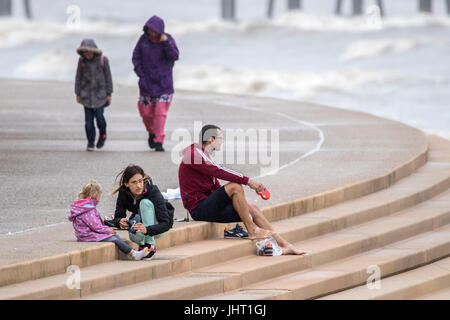 Blackpool, Lancashire, 15th July 2017. UK Weather.  Bad summer weather doesn't deter these holidaymakers from having a good time down at the beach on Blackpool seafront.  Heavy rain is expected to last all day with a chance of some brighter spells in the early evening.  Credit: Cernan Elias/Alamy Live News Stock Photo