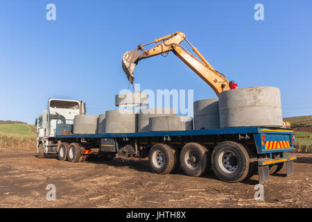 Truck loaded with new concrete drain water pipes waste casting sections  unloading on countyside construction site. Stock Photo