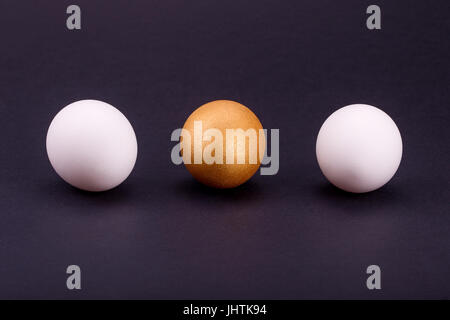 one golden egg with two white on black background. Stock Photo