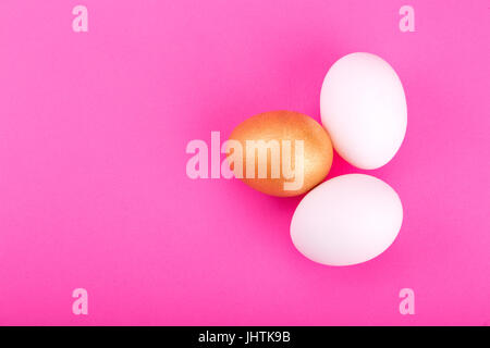 one golden egg with two white on pink background. Stock Photo