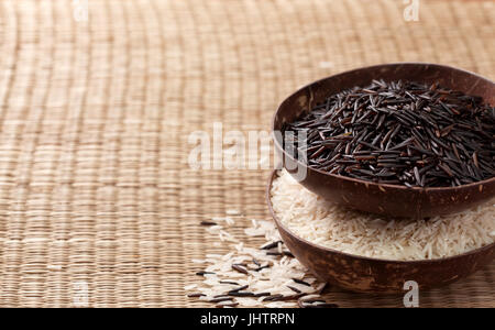 Black wild rice and basmati rice in bowls on a straw background Stock Photo