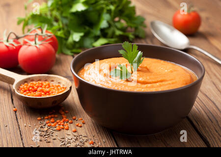Soup puree of red lentils in a brown bowl, fresh tomatoes, parsley on an old wooden background Stock Photo