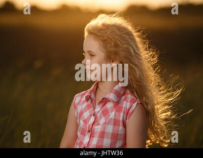 Little blonde child girl standing in summer field at sunset. Stock Photo