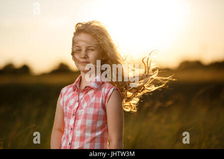 Little blonde child girl standing in summer field at sunset. Stock Photo