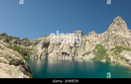 Dramatic rock formations surrounding the turquoise Lac de Capitello in the mountains above Restonica near Corte in Corsica Stock Photo