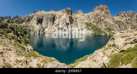 Dramatic rock formations surrounding the turquoise Lac de Capitello in the mountains above Restonica near Corte in Corsica Stock Photo