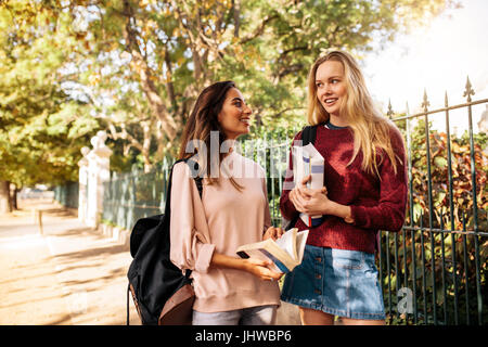 Young female students with books talking on the road. Beautiful women walking outside the sidewalk. Stock Photo