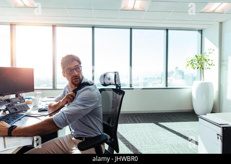 Businessman working in his office with computers and business papers on table. Young entrepreneur looking behind holding the receiver while on call at Stock Photo