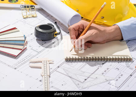 Working on blueprints. Construction project with hands writing on notebook. Stock Photo