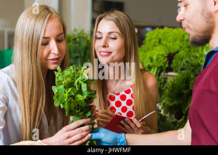 The seller and two blonde women at a vegetable market. Girlfriends buy vegetables on the market. Stock Photo