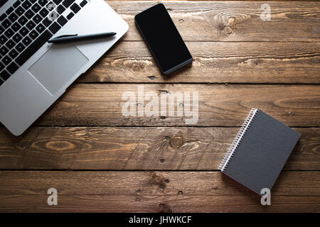 Top view of open laptop, mobile and notepad, ready to work standing on the wooden table Stock Photo